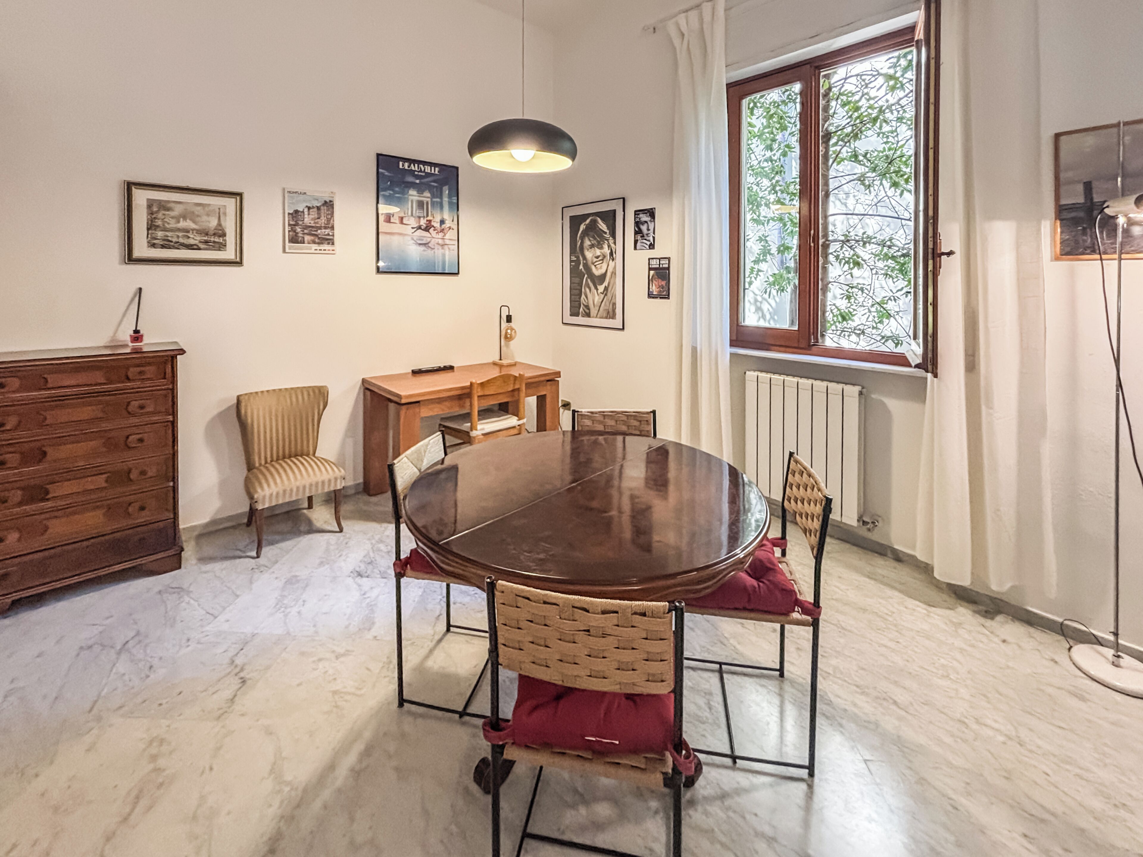A dining area with a round table, chairs, a wooden dresser, and a window with a view.