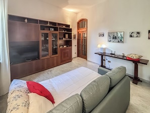 A bedroom with a bed, a sofa, a wooden cabinet, a desk with a lamp, and framed pictures on the wall.