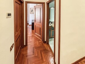 A hallway with wooden flooring, a door, and a view into a kitchen area with cabinets and a sink.