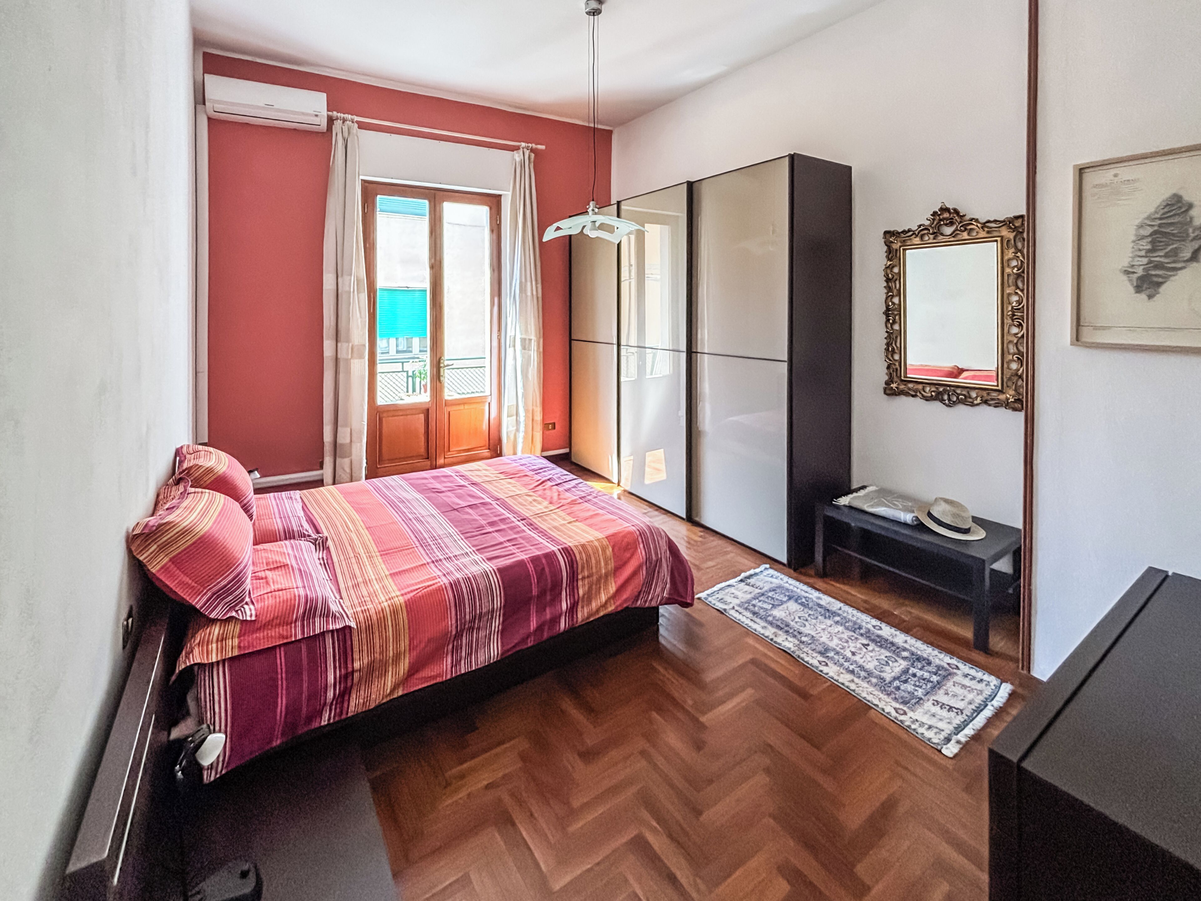 Une chambre à coucher avec un lit, une armoire, un miroir et une fenêtre avec des rideaux.