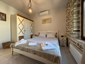 Un dormitorio con cama, mesitas de noche, armario, pared de piedra y ventana.