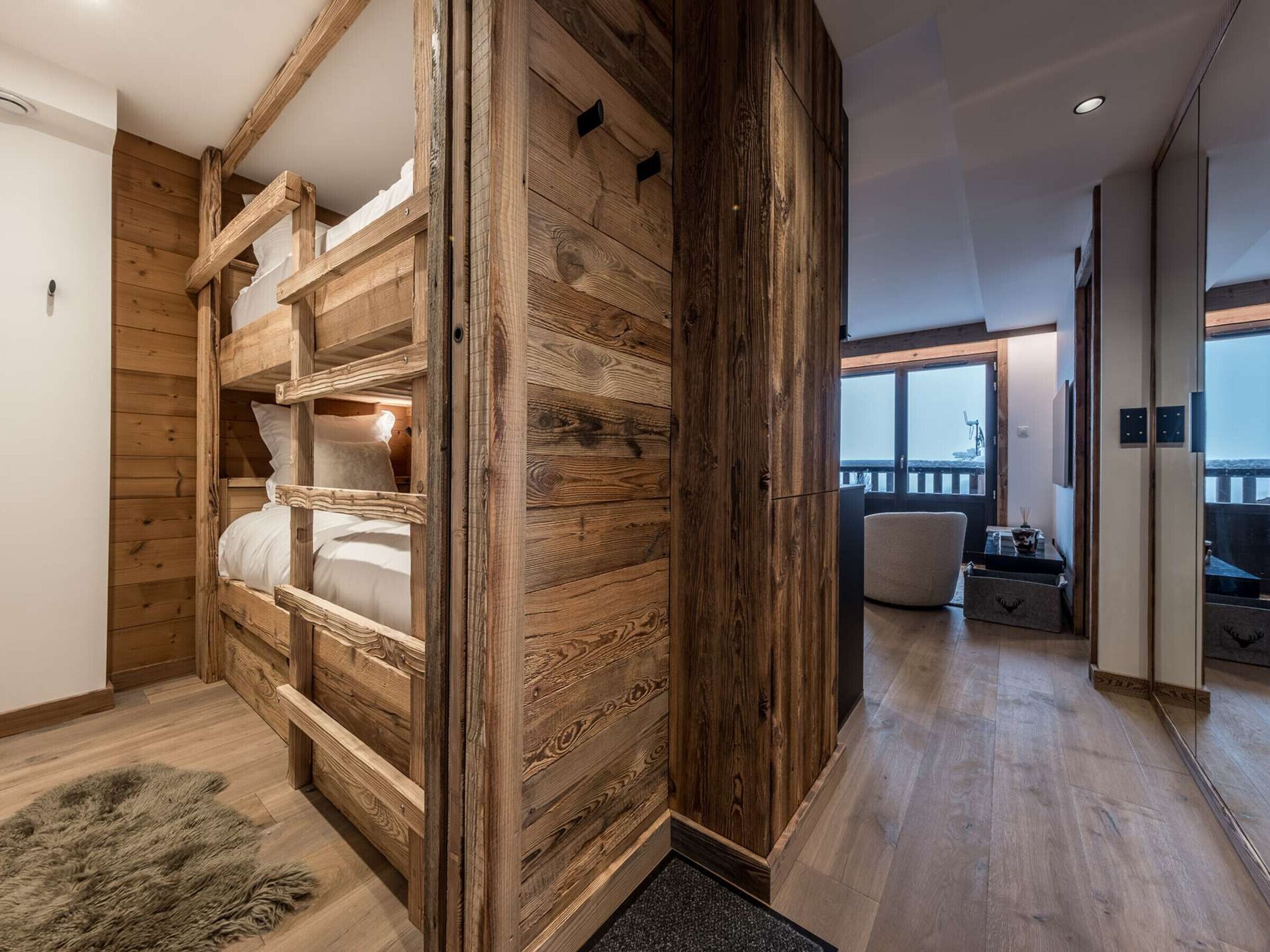 Ein Zimmer mit einem Etagenbett, Holzwänden, Blick ins Freie und einer Sitzecke mit Tisch.