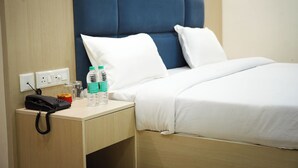 Une chambre d’hôtel avec un lit, une table de chevet avec un téléphone, une bouteille d’eau et une tasse.