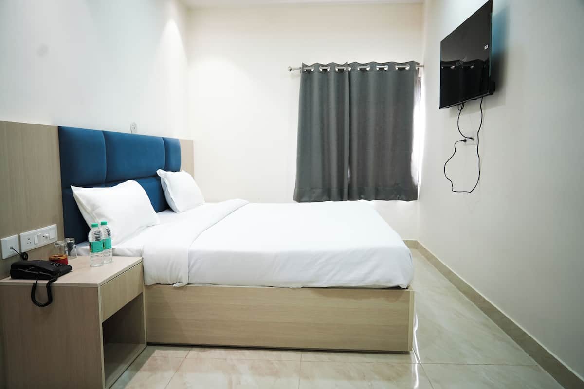 A hotel room with a bed, bedside table, phone, and a TV mounted on the wall.