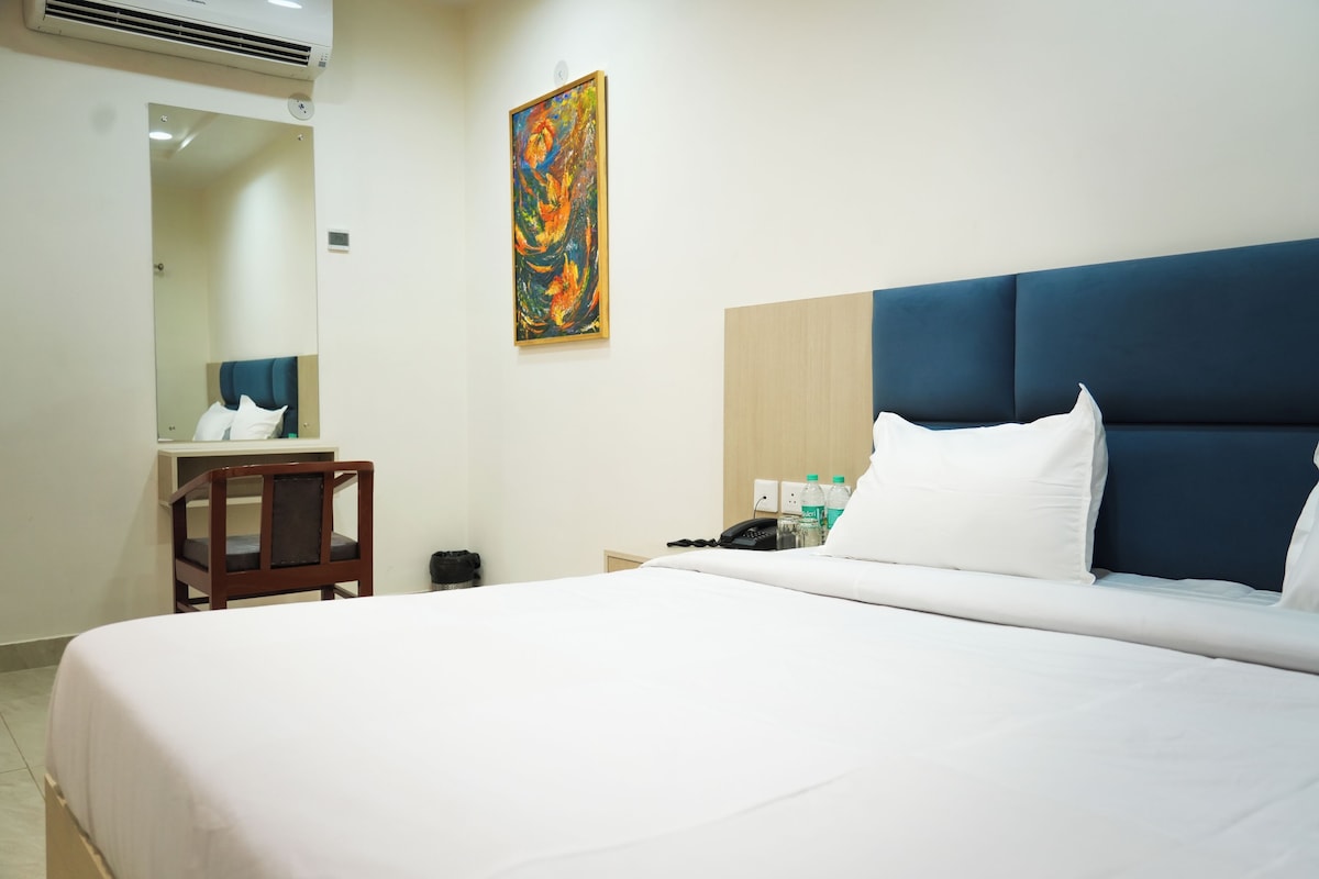 Quarto de hotel com uma cama grande, uma cadeira de madeira, uma escrivaninha, um telefone e um quadro na parede.