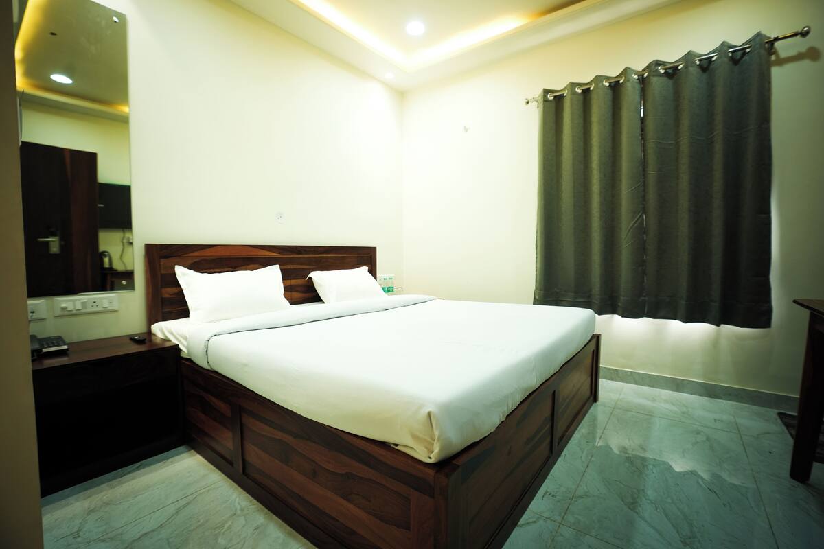 A neatly made bed in a room with a wooden headboard, a nightstand, a mirror, and a window with curtains.
