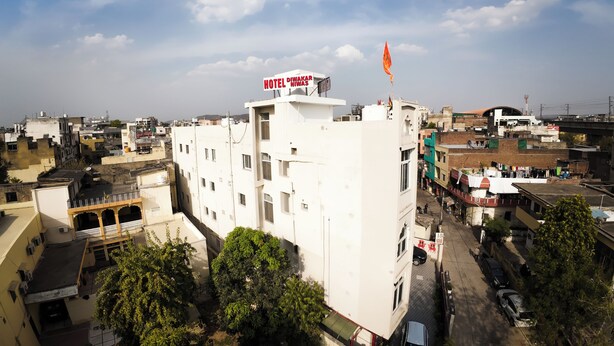 Un hôtel à plusieurs étages, surmonté d’un drapeau sur son toit, entouré d’autres bâtiments et d’arbres.