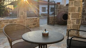 Eine Terrasse mit Steinboden, einem runden Tisch und zwei Stühlen, ein roter und ein brauner, mit Sonnenuntergang im Hintergrund.
