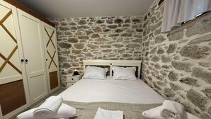 Ein Schlafzimmer mit Steinwand, einem Bett mit weißen Leinen und einem Schrank mit geometrischem Muster.