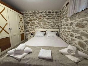 A bedroom with a stone wall, a bed with white linens, and a wardrobe with a geometric design. - White Stone Apartments - Ground Floor (Sithonia)