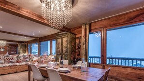 A dining area with a wooden table set for four, surrounded by chairs, with a large window offering a view of a snowy landscape. - Courchevel 1850 - 65m² Apt - 4 Guests - Ski-in/Ski-out - Center (Courchevel)