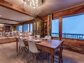 A dining area with a wooden table set for four, surrounded by chairs, with a large window offering a view of a snowy landscape. - Courchevel 1850 - 65m² Apt - 4 Guests - Ski-in/Ski-out - Center (Courchevel)