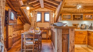 Une cuisine rustique avec des poutres en bois, un coin repas avec une table et des chaises, et un plan de travail équipé d’appareils électroménagers.