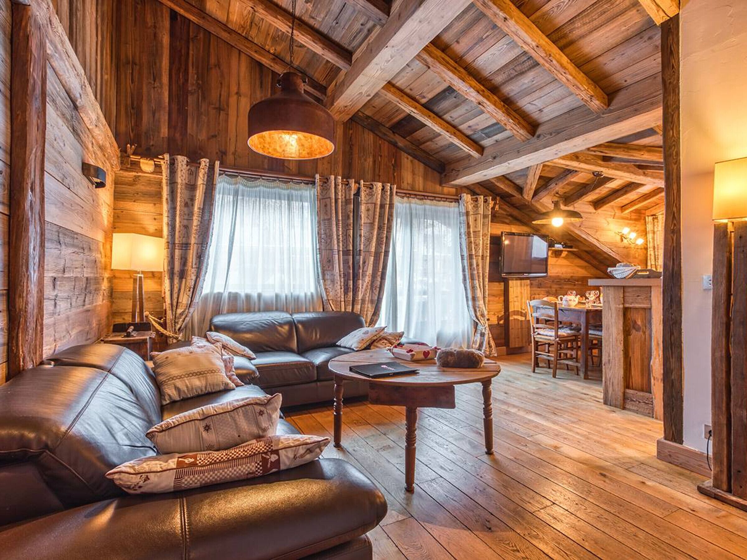 Ein gemütliches Blockhaus-Interieur mit einem Ledersofa, einem Holztisch und einem Essbereich mit Fernseher.