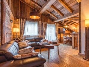 A cozy log cabin interior with a leather sofa, a wooden coffee table, and a dining area with a TV. - Charming 81m² Apt in Courchevel 1850 - Central, Near Slopes, Sleeps 4, Balconies, Luxury Amenities (Courchevel)