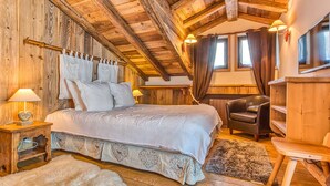 Une chambre confortable avec un plafond en bois, un lit avec une literie blanche, une chaise et un téléviseur.