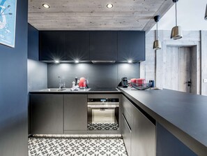 A modern kitchen with dark cabinets, a black countertop, and a patterned tile floor. - Central Courchevel 1550 apartment, 6/7 people, Wi-Fi, parking, spa access (Courchevel 1550)