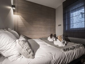 A modern bedroom with a wooden headboard, a large window, and a neatly made bed with pillows and a blanket. - Cozy 51m² Apt, Sleeps 4 - Central Courchevel, Near Slopes, Fireplace, Balcony, Spa Access (Courchevel 1550)