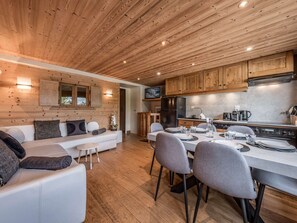 Eine moderne Küche mit Holzausstattung, ein Essbereich mit Tisch für vier Personen und ein Wohnbereich mit Sofa und Kissen.