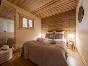 Ein gemütliches Schlafzimmer mit Holzboden, einem Bett mit vielen Kissen, einem Nachttisch mit Lampe und einem Fenster mit Vorhängen.