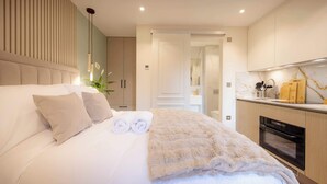A modern hotel room with a large bed, a kitchen area, and a bathroom visible through an open door. - Premium Studio 5 at The Orange Door Little Venice (Greater London)
