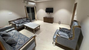 Ein Wohnzimmer mit einer Sofagarnitur, einem Couchtisch, einem an der Wand befestigten Fernseher und einem Deckenventilator.