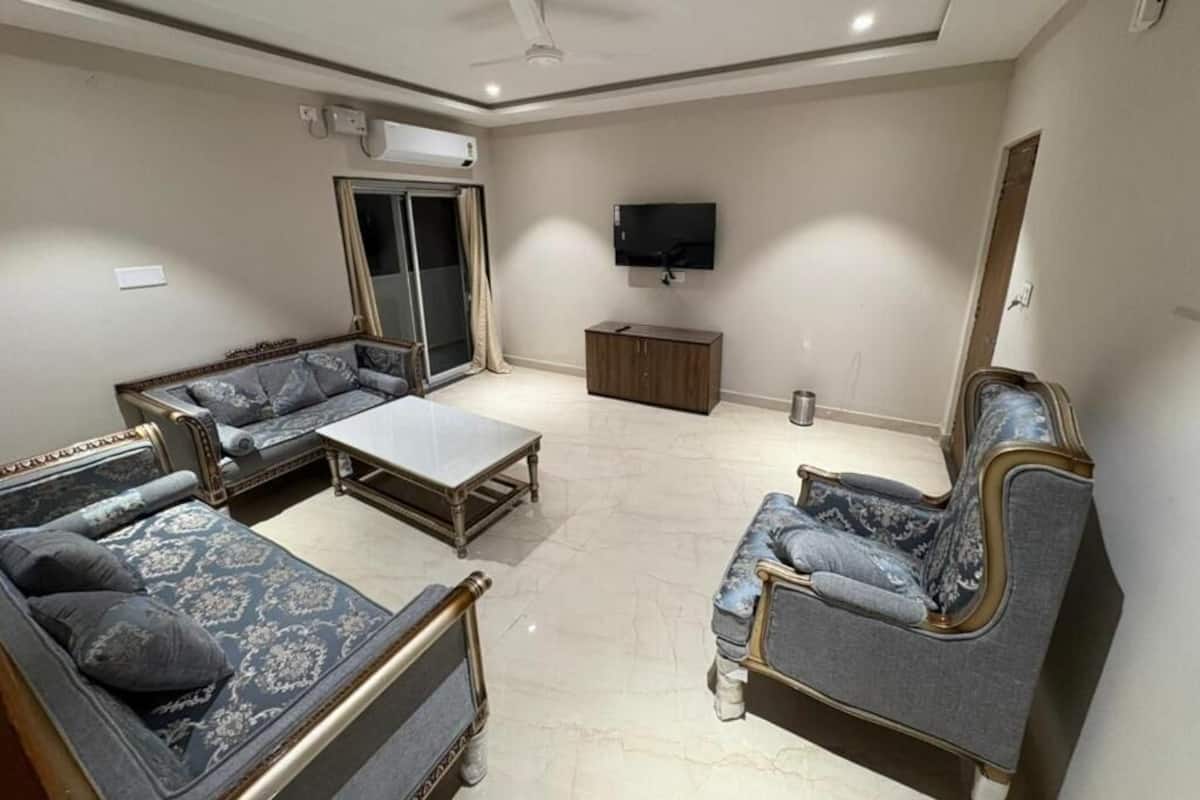 A living room with a sofa set, a coffee table, a TV mounted on the wall, and a ceiling fan.