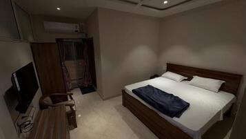 Um quarto com cama, escrivaninha, cadeira e televisão.