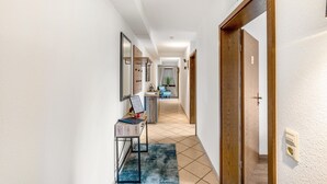 Um corredor com uma escrivaninha, um espelho e uma porta que dá para outro quarto.
