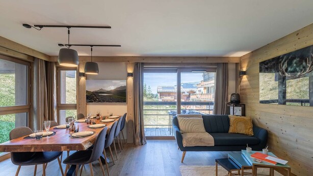 Un interior moderno con comedor, sofá y ventanas amplias que ofrecen vistas al exterior.
