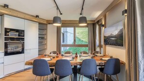 Una cocina moderna con electrodomésticos integrados, un comedor con mesa y sillas de madera, y un ventanal con vistas a zonas verdes.