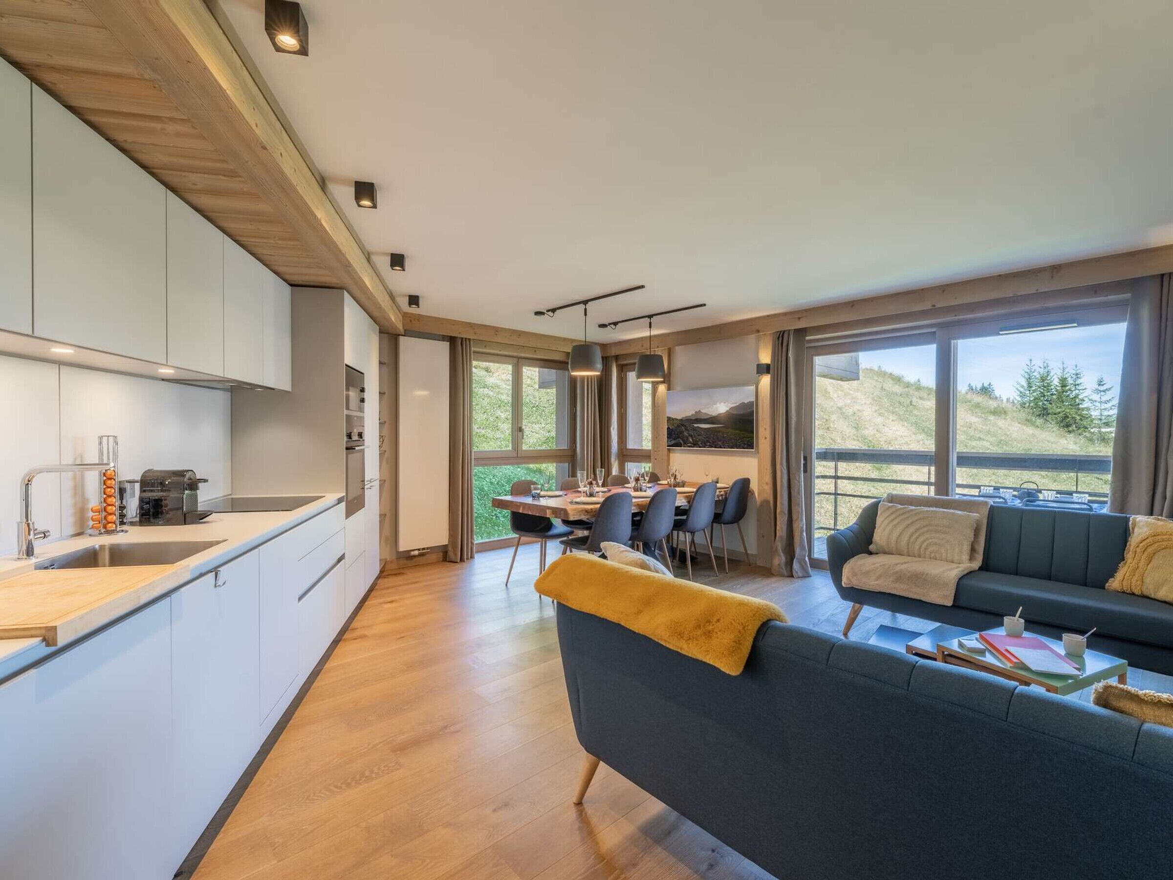 Eine moderne Küche mit Essbereich, einer Couch und großen Fenstern mit Blick ins Freie.