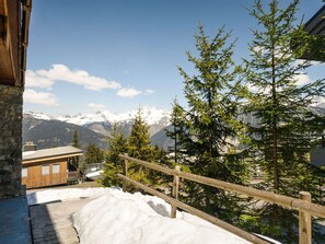 Eine Holzterrasse mit Schnee, Blick auf einen Berg und ein Gebäude mit einer Steinfassade.