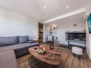 Ein modernes Wohnzimmer mit grauem Sofa, einem Couchtisch mit Obst, einem Kamin und einer Küche im Hintergrund.