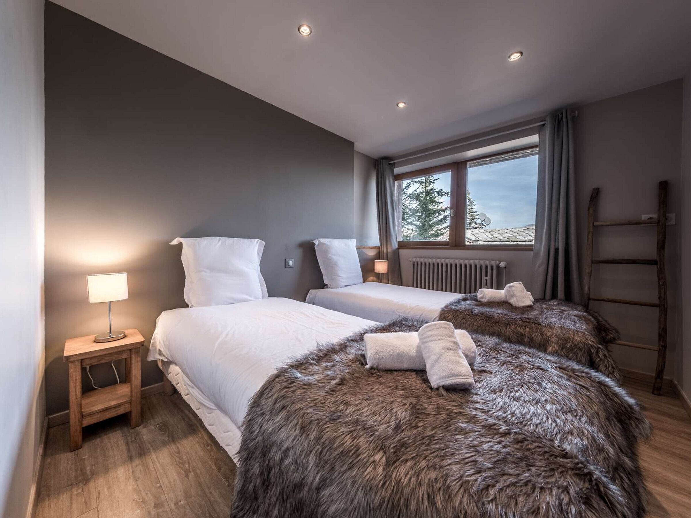 Ein modernes Hotelzimmer mit zwei Betten, einem Fenster mit Blick, einem Holzboden und einem kleinen Nachttisch mit Lampe.