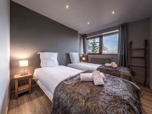 Ein modernes Hotelzimmer mit zwei Betten, einem Fenster mit Blick, einem Holzboden und einem kleinen Nachttisch mit Lampe.