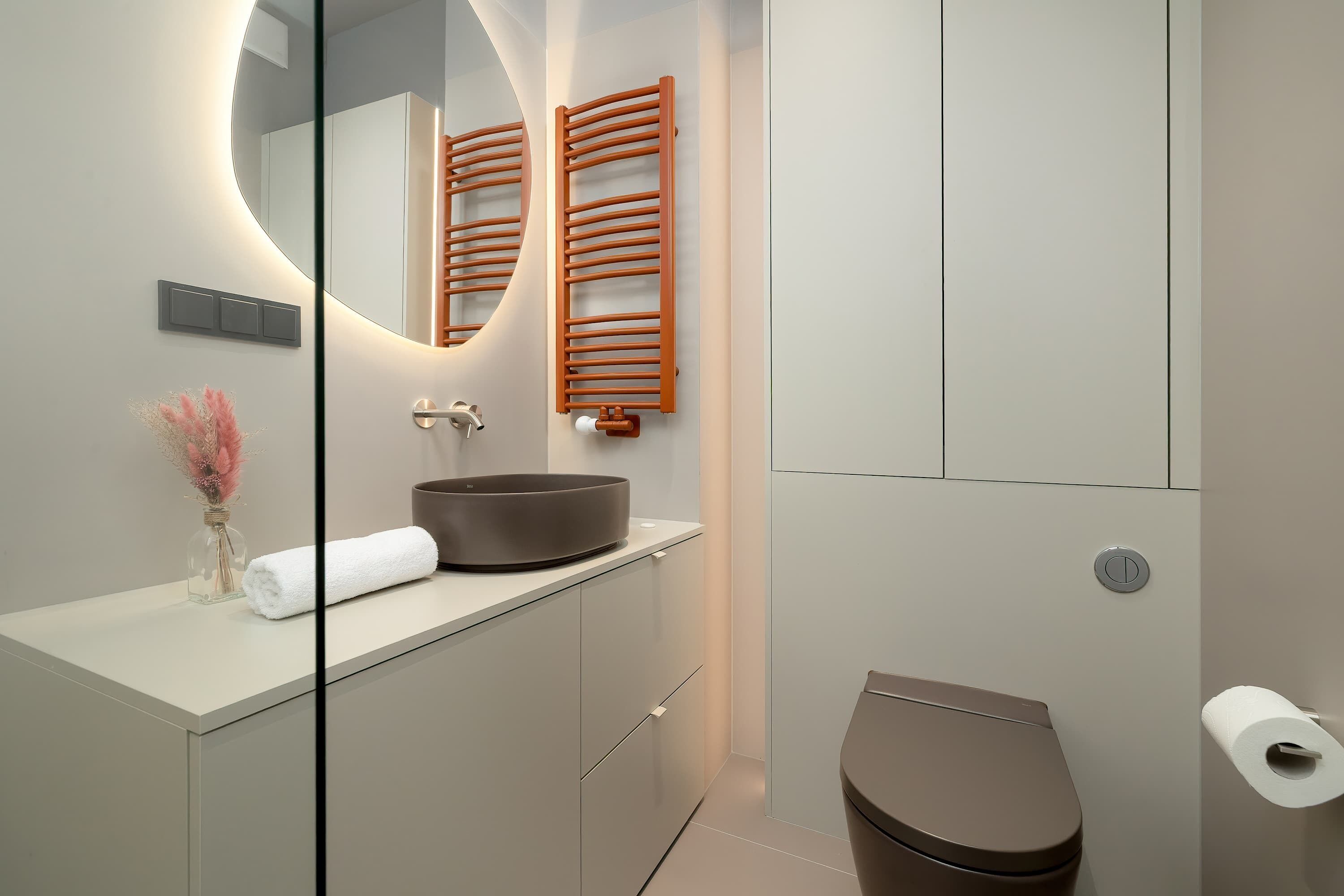 Un baño moderno con un espejo redondo, toalleros de madera, un lavabo sobre encimera y un inodoro.
