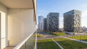 A modern building with large windows, a glass railing, and a view of a cityscape with high-rise buildings.