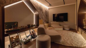 A modern bedroom with a sloped ceiling, a large bed, a TV, and a desk with toys.