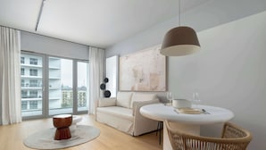 A modern living room with a sofa, a round dining table, a wicker chair, a round coffee table, and a large abstract painting on the wall.