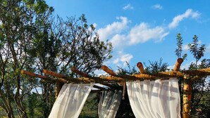 Un espace aménagé au bord de la piscine, avec une pergola recouverte d’un tissu blanc, un chemin en pierre et une piscine à l’eau d’un bleu limpide.