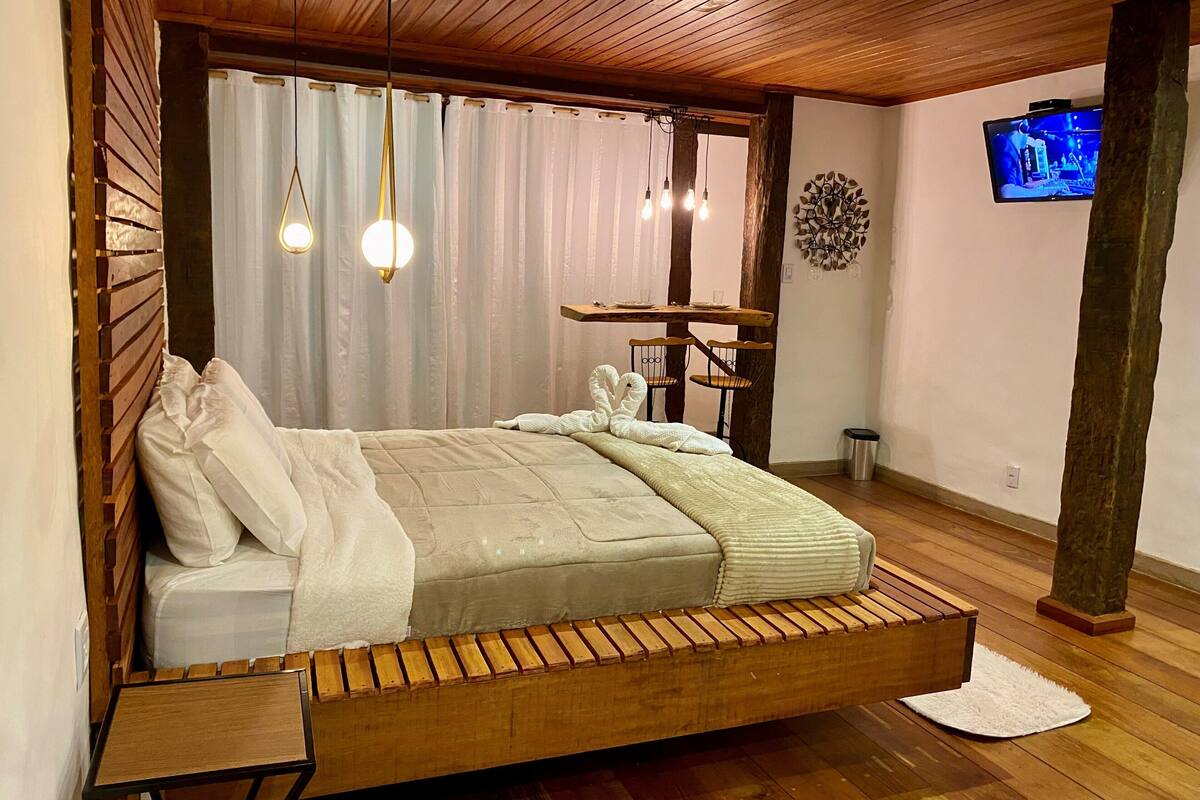 Un dormitorio moderno con una cama de listones de madera, una mesita pequeña y un televisor montado en la pared.
