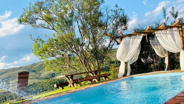Une piscine bordée de pierres, une terrasse en bois et un arbre décoré de guirlandes blanches.