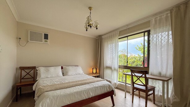 Un dormitorio con cama, escritorio, silla, ventana con cortinas y lámpara en el techo.