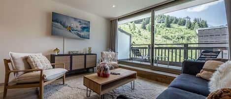 Una sala de estar moderna con un ventanal grande, un sofá, una mesa de centro y un televisor montado en la pared.