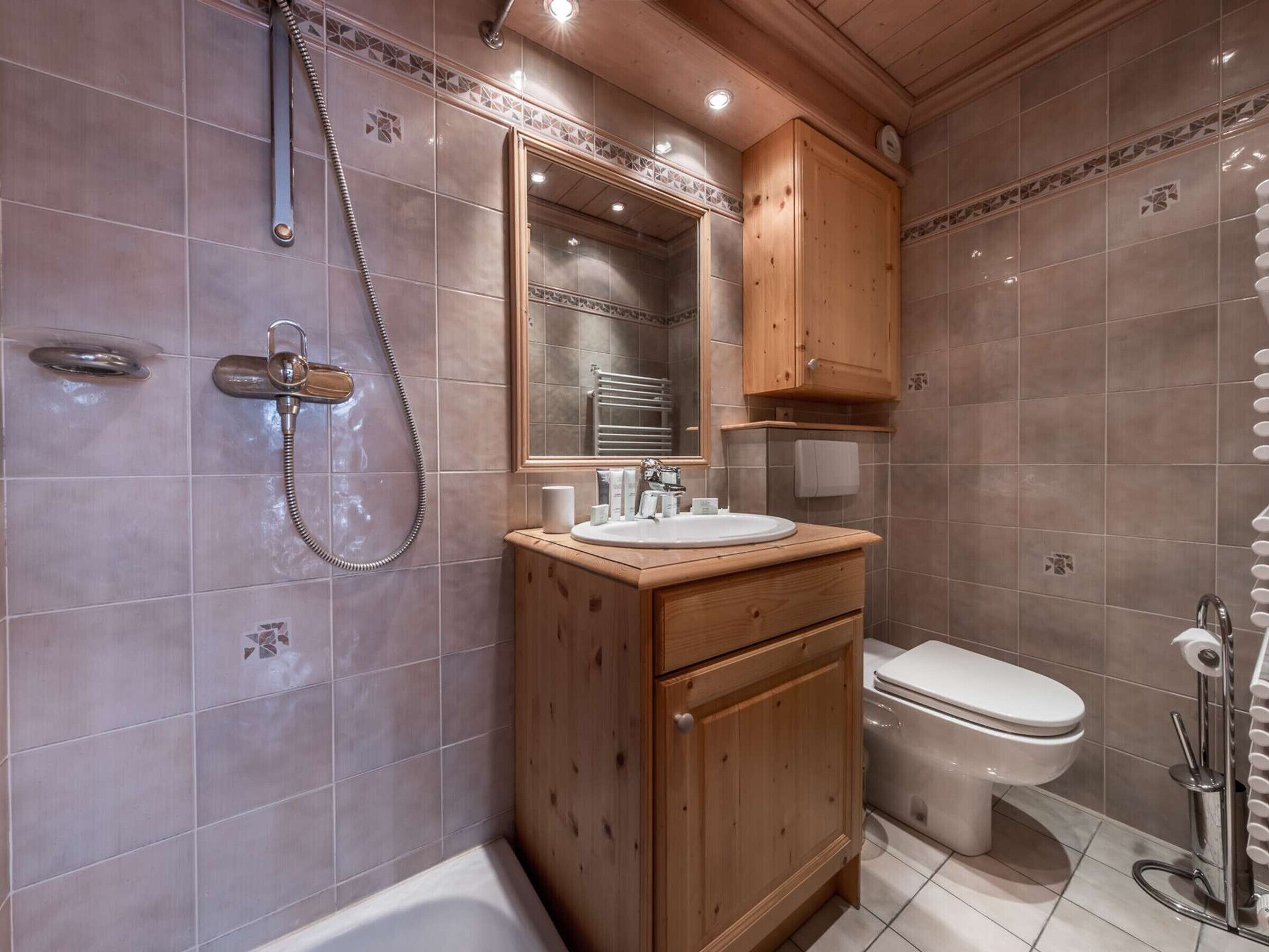 Een badkamer met een douche, toilet en een houten wastafelmeubel met spiegel.