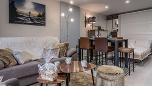 Una sala de estar moderna con sofá, mesa de centro, reposapiés, mesa de comedor, sillas y un cuadro en la pared.