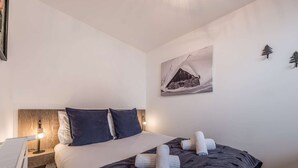 Un dormitorio con cama, almohadas, una mesita de noche, lámpara y un cuadro en la pared.