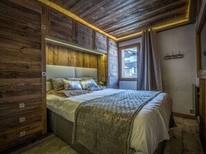 Ein Schlafzimmer mit Holzwänden, einem Bett, einem Nachttisch und einem Fenster mit Vorhängen.
