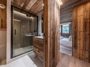 A modern bathroom with a glass shower enclosure, wooden vanity, and a visible bedroom with a bed and window. - Duplex Ski in/out 5 pers, 2 bed, 3 bath, Balcony, WIFI - Courchevel 1650 (Courchevel 1650)